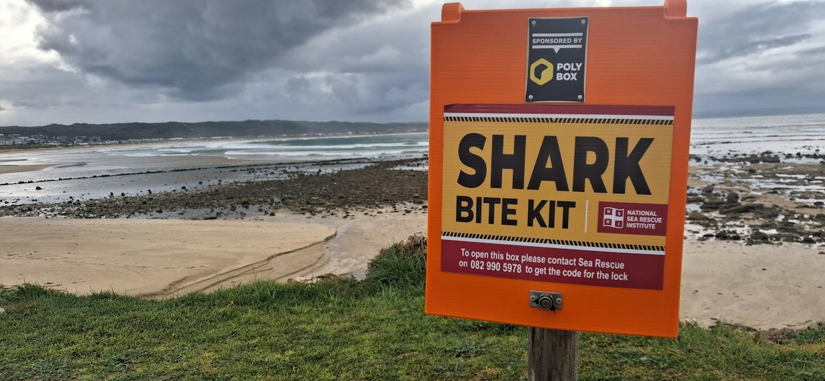 An orange sign reading SHARK BITE KIT on a post overlooking a sandy beach